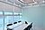 Modern conference room with a large white table, black chairs, and large windows featuring blinds. Bright, minimalist design.