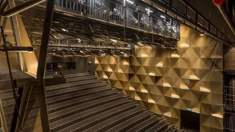 Interior of a modern theater featuring tiered seating, a geometric wall design, and overhead lighting and rigging systems.