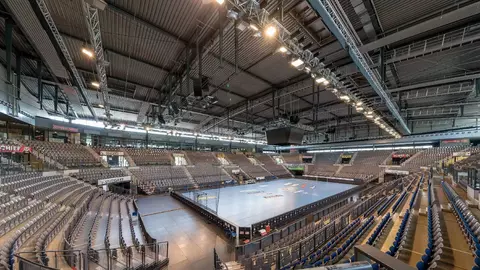 Indoor sports arena with empty seating and a central court area, featuring overhead lighting and a spacious layout.