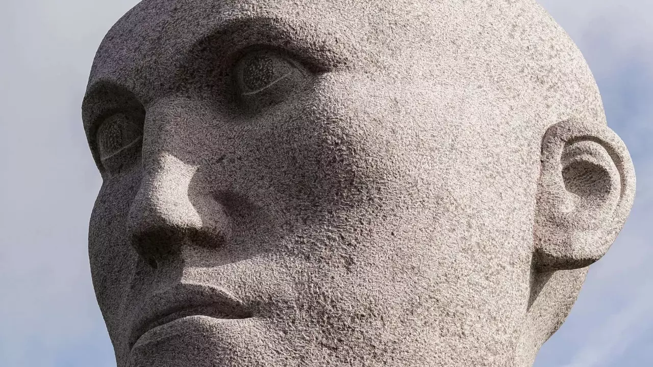 Granite sculpture of a stylized human head, featuring a smooth surface and a serious expression, against a cloudy sky.