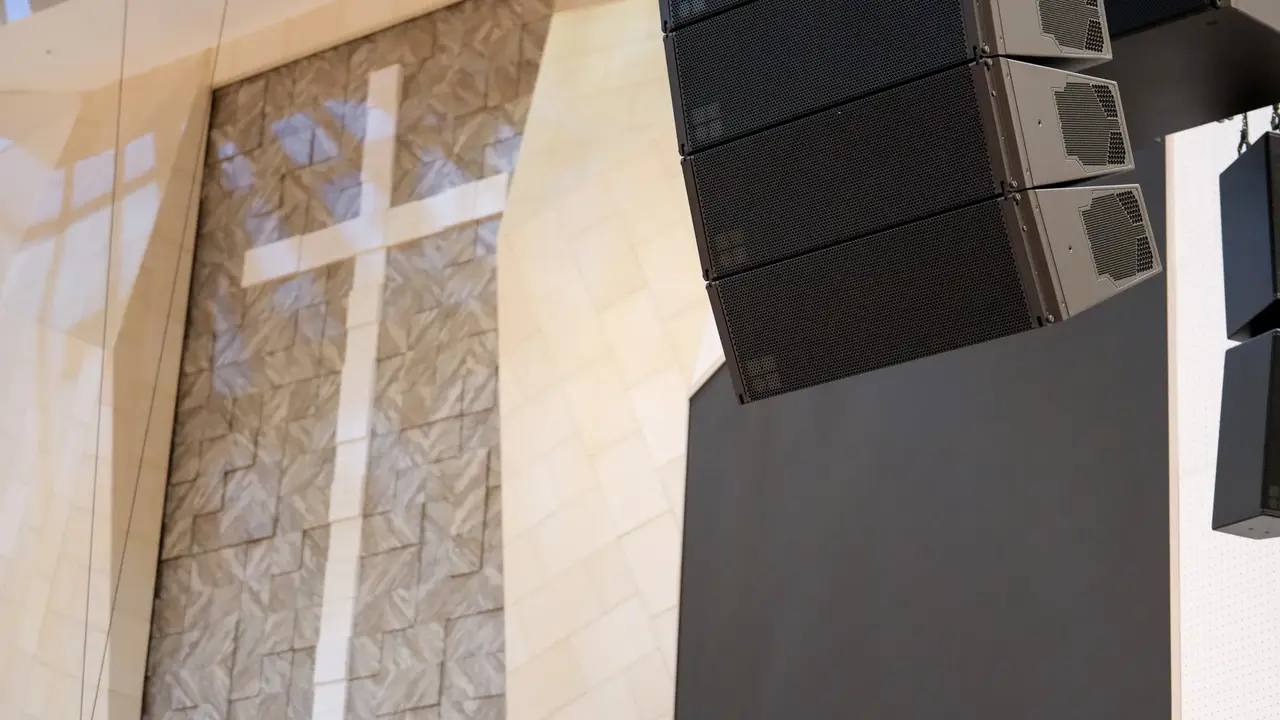 Large speakers are mounted near a textured wall featuring a prominent cross, illuminated by soft lighting.