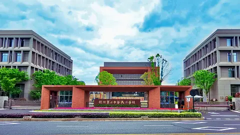 Modern educational institution with a prominent entrance, flanked by two large buildings and greenery, under a partly cloudy sky.