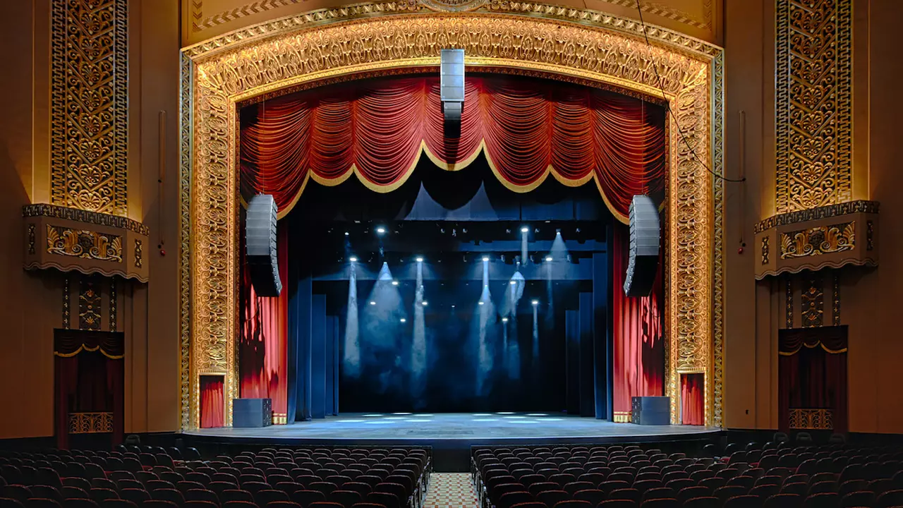 Theater stage with red curtains and ornate golden detailing, illuminated by stage lights, ready for a performance.