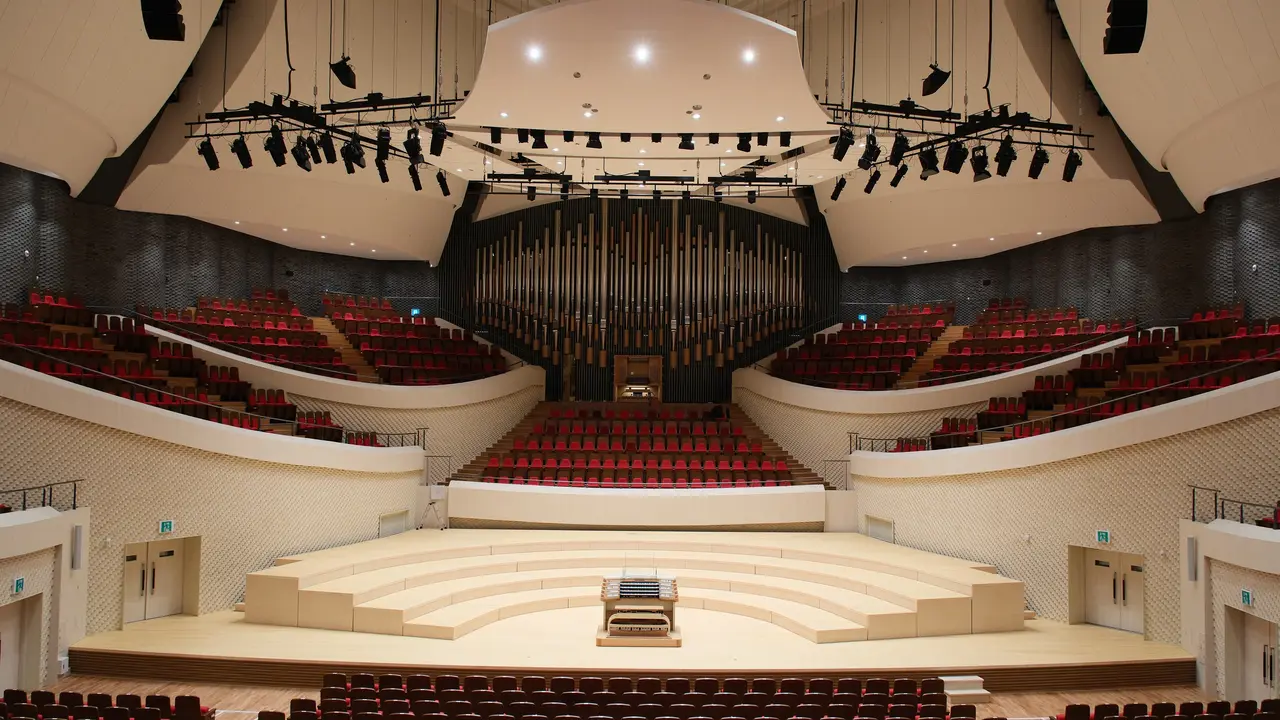 Concert hall featuring tiered seating, a central stage, and a large pipe organ at the rear. The design emphasizes acoustics and visibility.
