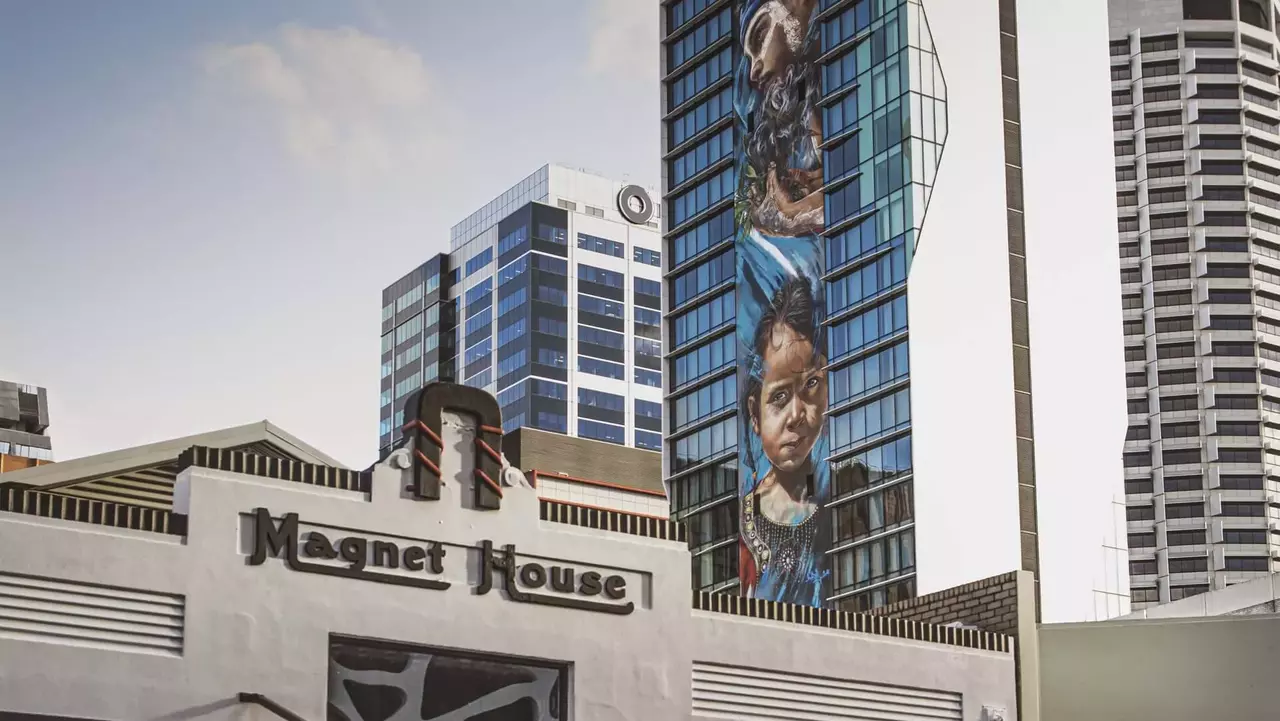 Magnet House building with a large mural of a child on the adjacent skyscraper, featuring modern architecture in an urban setting.