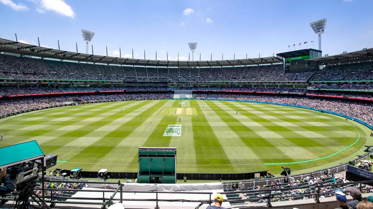A panoramic view of a cricket stadium filled with spectators, featuring a well-maintained pitch and vibrant green outfield under a clear blue sky.