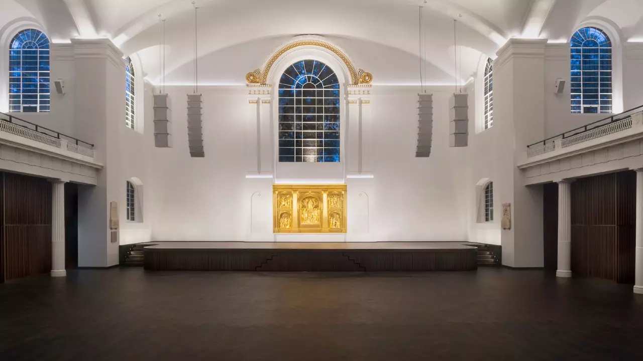 Interior of a spacious, modern church featuring a large golden altar, tall windows, and a minimalist design with wooden accents.