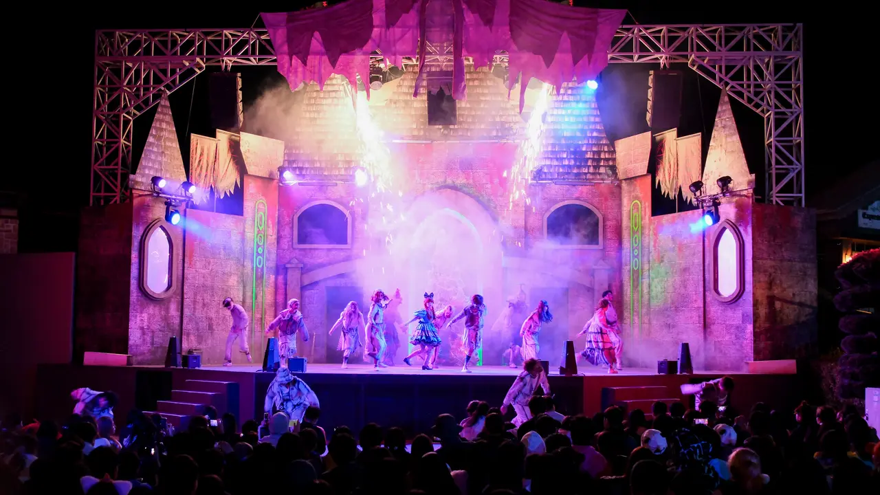 A theatrical performance featuring dancers in colorful costumes on stage, with dramatic lighting and special effects, in front of an audience.