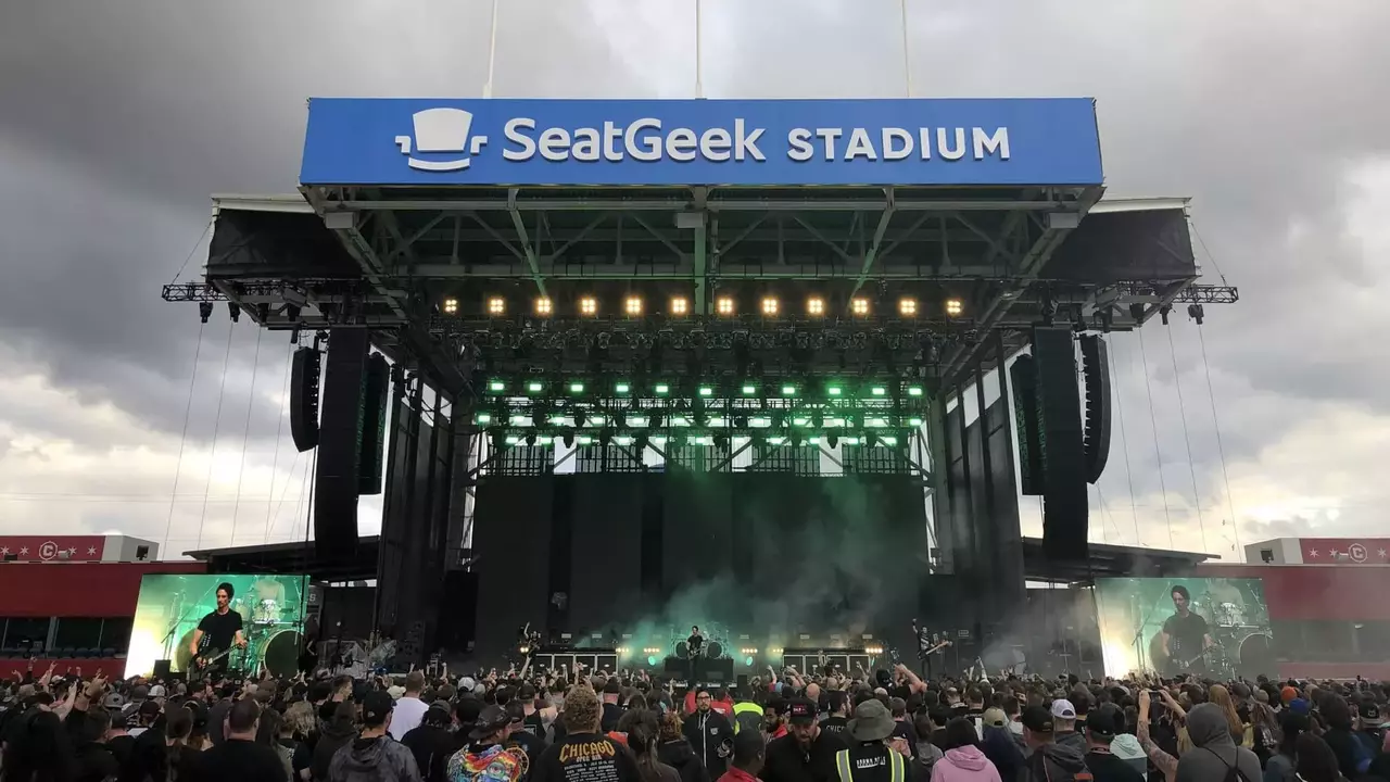 Crowd gathered at SeatGeek Stadium for a live performance, with a large stage featuring green lighting and a cloudy sky overhead.