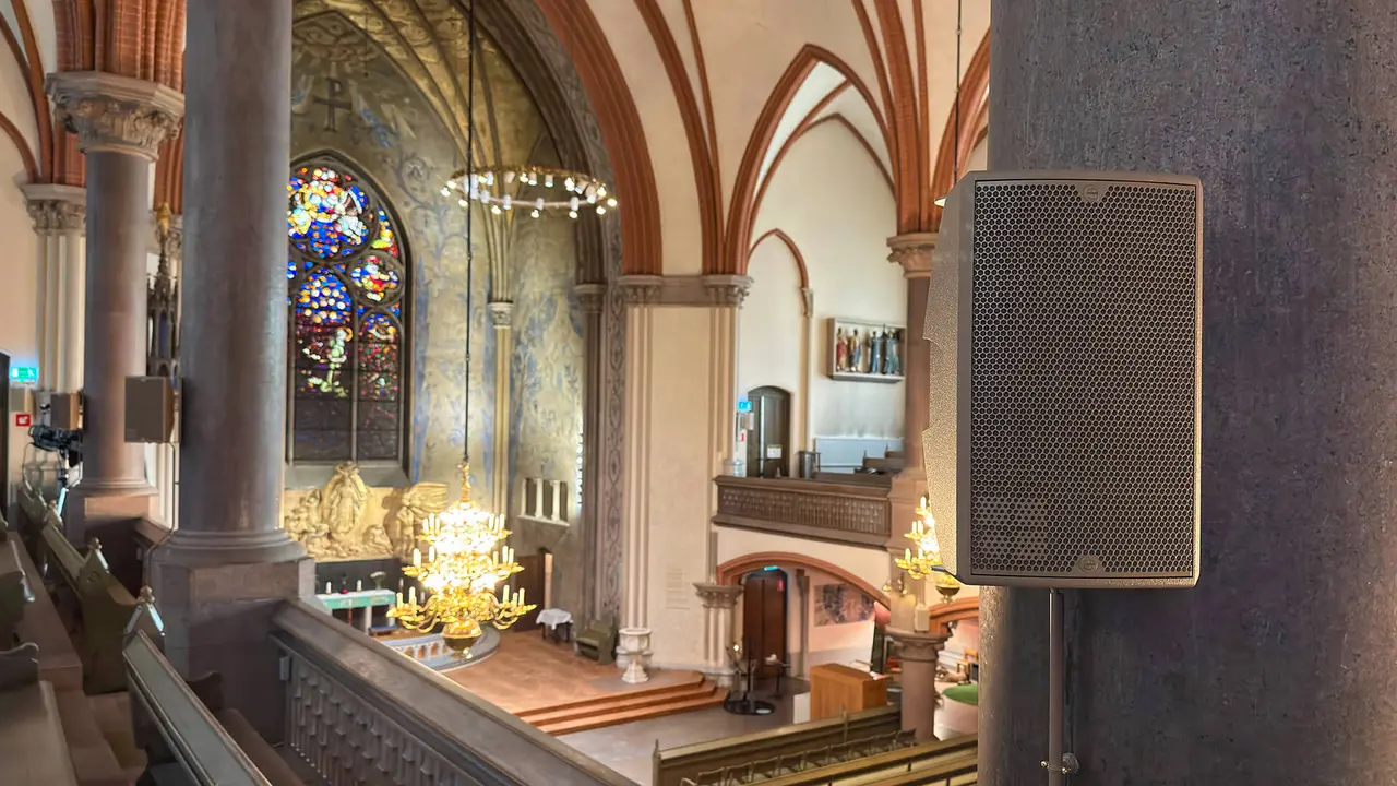 Interior of a church featuring stained glass windows, ornate chandeliers, and a sound speaker mounted on a pillar.