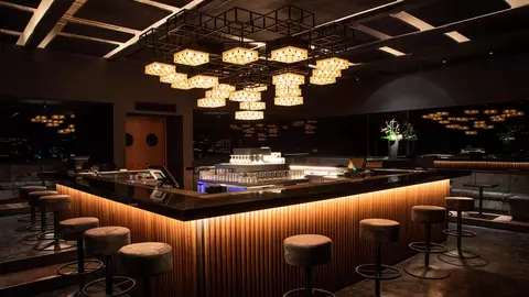 Modern bar interior featuring a sleek counter, stylish stools, and unique pendant lighting, creating a sophisticated atmosphere.