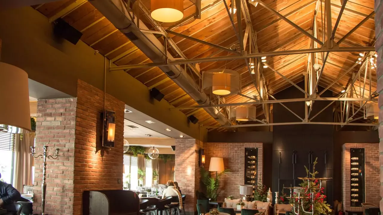 Modern restaurant interior featuring exposed wooden beams, brick walls, and a mix of seating arrangements. Soft lighting enhances the ambiance.