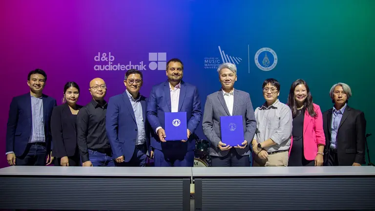 Group of professionals standing together, holding documents, with logos of d&b audiotechnik and Music Matters in the background.