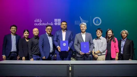 Group of professionals standing together, holding documents, with logos of d&b audiotechnik and Music Matters in the background.
