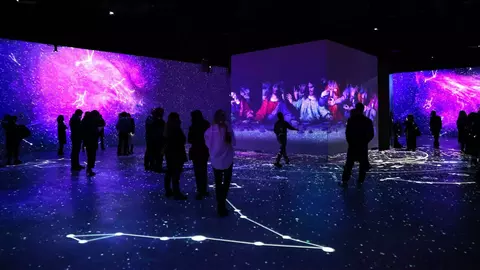Visitors explore an immersive art installation featuring vibrant projections of stars and historical artworks on walls and floors.
