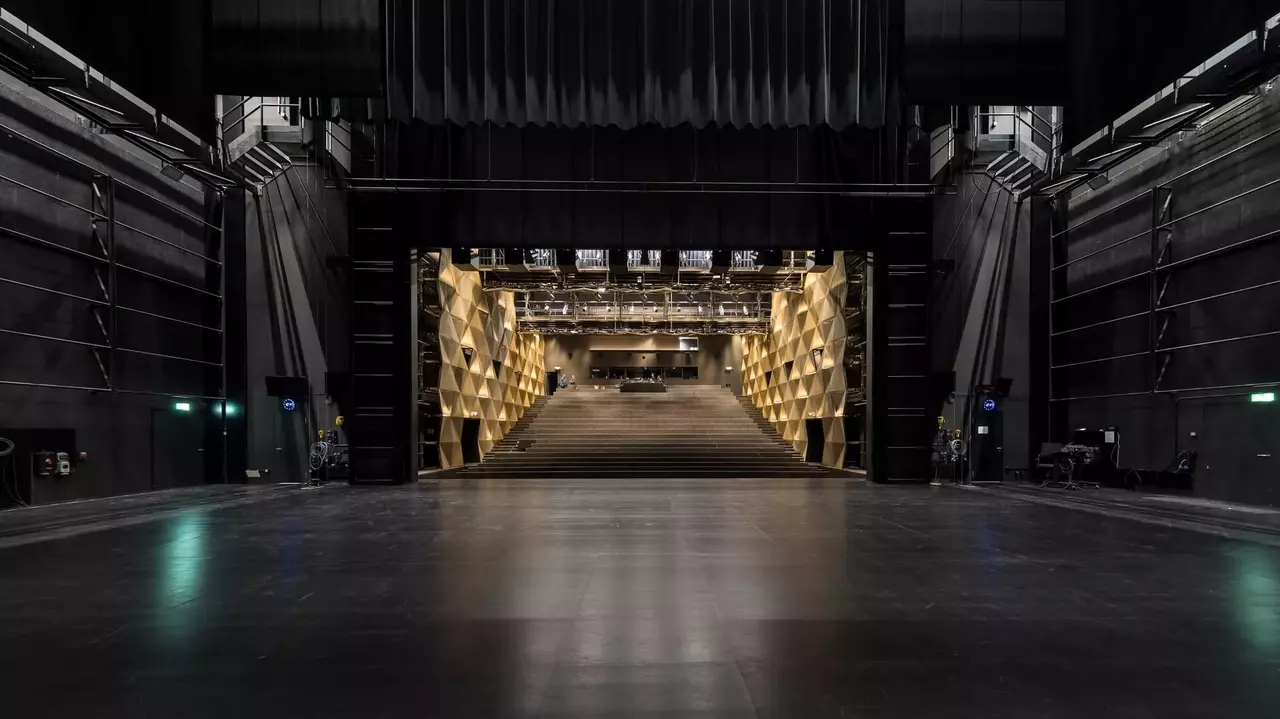 Empty theater stage with a view of a grand staircase leading to a well-lit auditorium, featuring a modern architectural design.