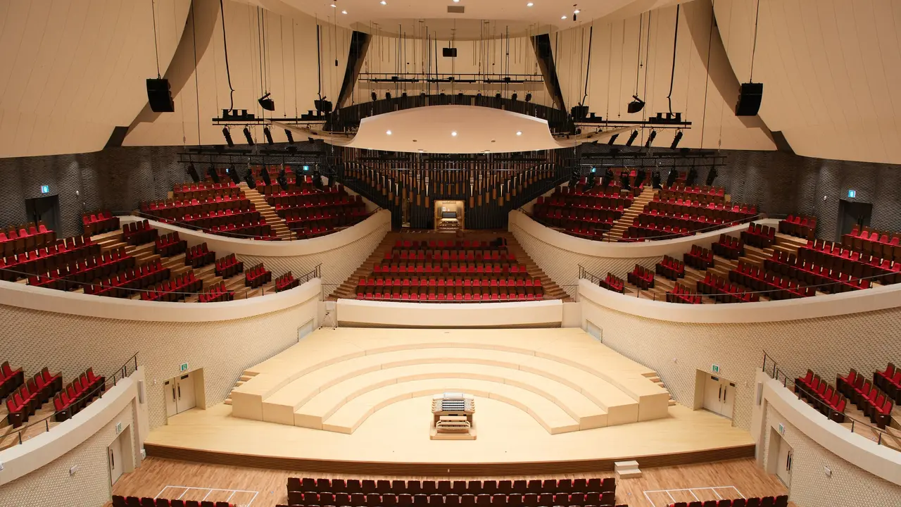 Concert hall interior featuring tiered seating, a central stage, and an organ, designed for performances and events.