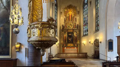 Interior of a church featuring a decorative pulpit, stained glass windows, and an ornate altar with religious artwork.