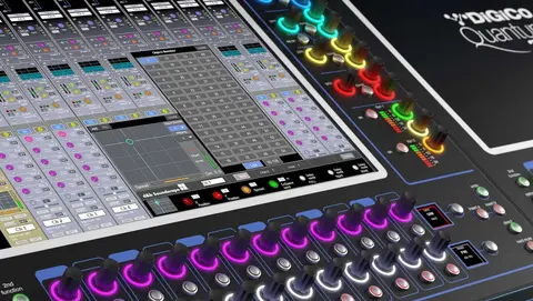 Digital audio mixing console with multiple faders, colorful LED indicators, and a touchscreen interface displaying various audio channels and settings.