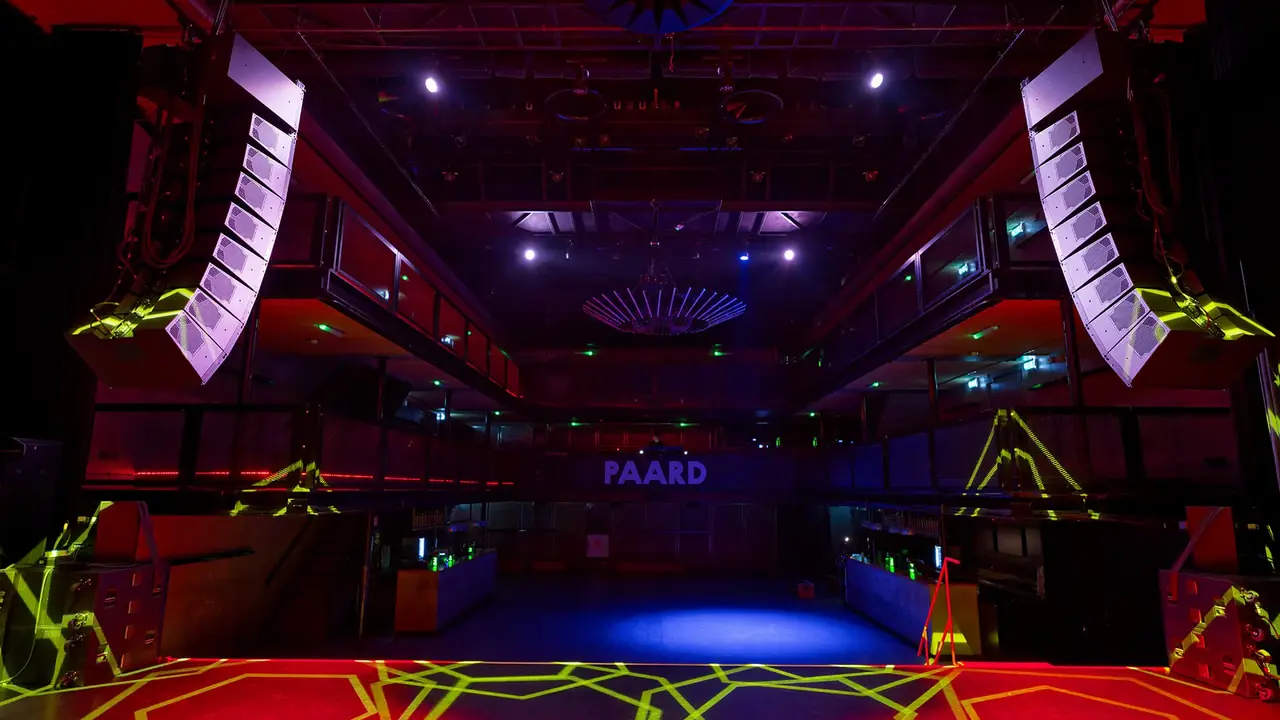 A vibrant music venue featuring colorful lighting, sound equipment, and a stage area with the name "PAARD" prominently displayed.
