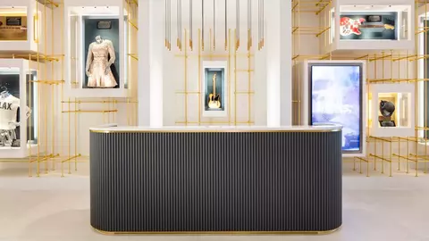 Modern reception desk in a stylish space, surrounded by display cases featuring various items, including clothing and musical instruments.