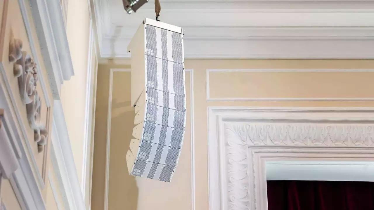 A curved sound speaker is mounted on the wall, designed for audio distribution in a room with ornate architectural details.