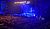 A large crowd attends a concert in a dimly lit venue, with bright stage lights illuminating musicians and a large screen displaying a performer.