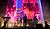 A performer stands in front of a large screen displaying vibrant visuals, accompanied by musicians playing instruments on stage.