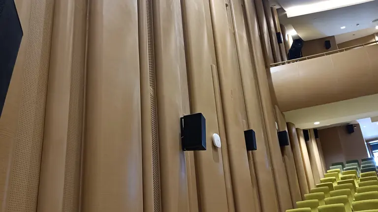 Interior view of a theater featuring textured brown walls, sound speakers, and green seating arranged in rows.