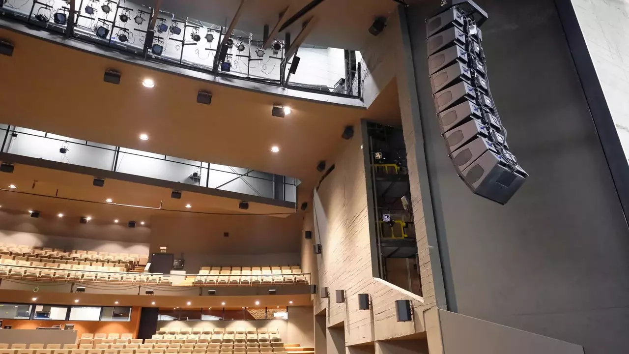 Interior of a theater featuring tiered seating and a large sound system suspended from the ceiling.