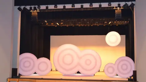 Stage setup featuring large, soft, circular structures in varying sizes and colors, illuminated under stage lights.