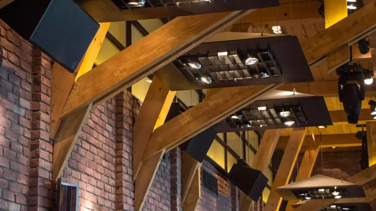 Wooden beams support modern light fixtures in a stylish interior, featuring a mix of brick walls and contemporary design elements.
