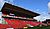 Stadium seating area with red seats and a large overhead roof, under a clear blue sky.