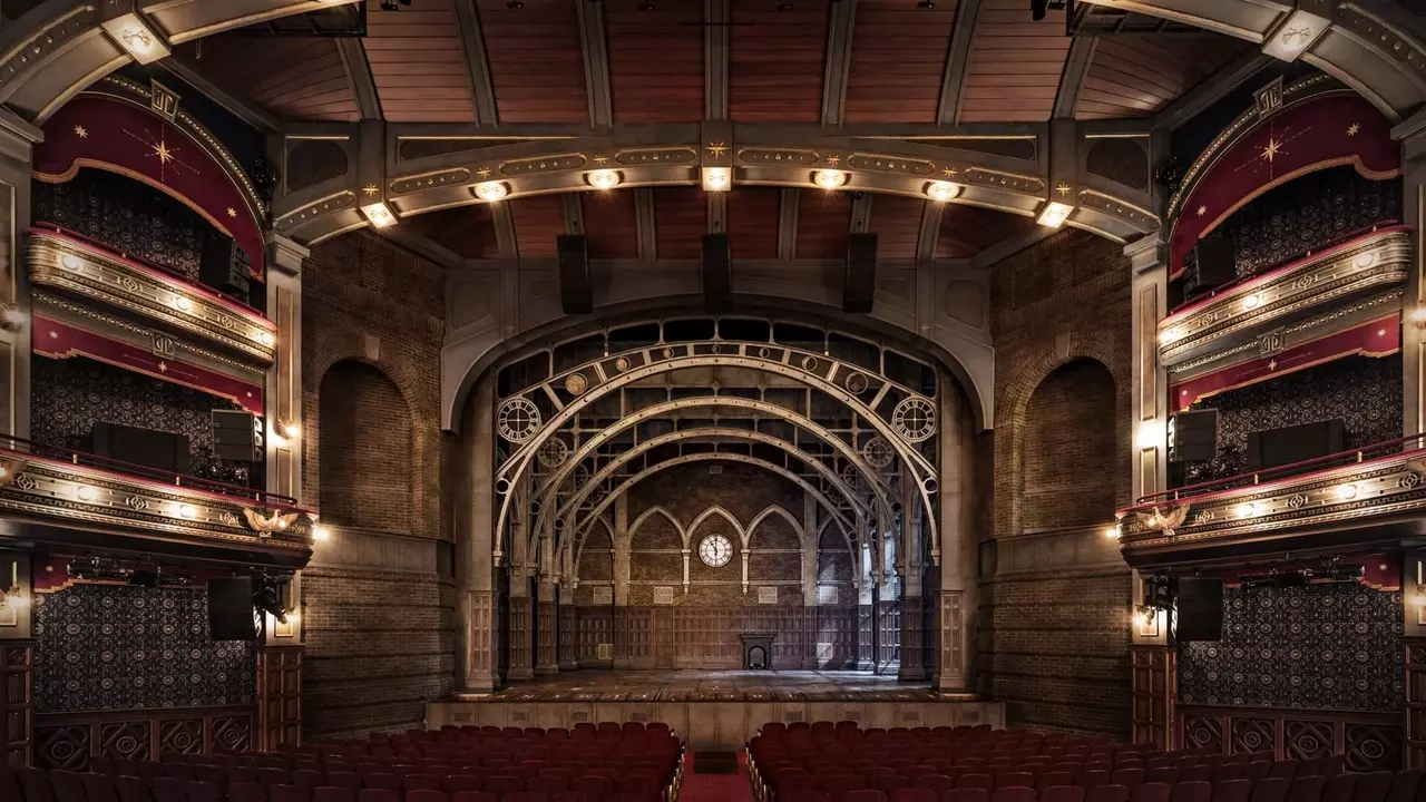Interior of a theater featuring ornate architecture, red seating, and a large stage with an arched backdrop.