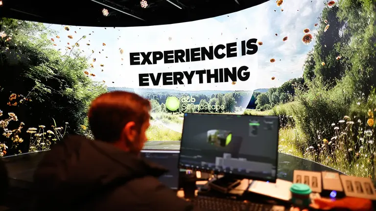 A person works at a computer in front of a large screen displaying the text "EXPERIENCE IS EVERYTHING" with a nature background.