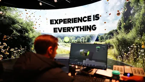 A person works at a computer in front of a large screen displaying the text "EXPERIENCE IS EVERYTHING" with a nature background.