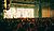 A crowded concert venue with a large illuminated backdrop, featuring a vibrant light display and a diverse audience enjoying the performance.