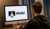 A person sits at a desk, facing a computer screen displaying the word "¡Hola!" alongside a user icon.