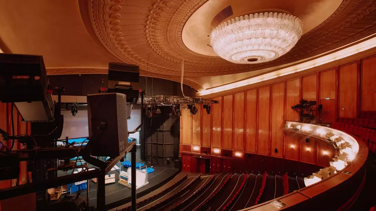 Interior view of a theater featuring a chandelier, wooden paneling, and seating arranged in a semi-circular layout.