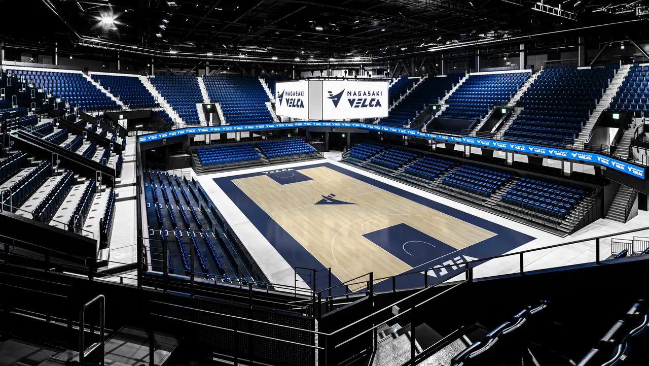 Indoor basketball arena featuring a polished court, surrounded by tiered seating and digital displays.