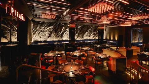 Modern restaurant interior featuring stylish seating, ambient lighting, and a decorative wall. Tables are set for dining.