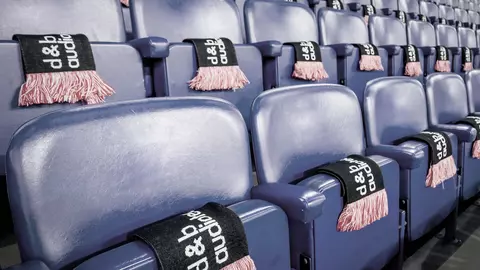 Empty stadium seats with black and pink branded seat covers displayed on the armrests.