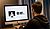 A person sits at a desk facing a computer screen displaying a simple icon of a user and the Chinese greeting "你好" (Hello).