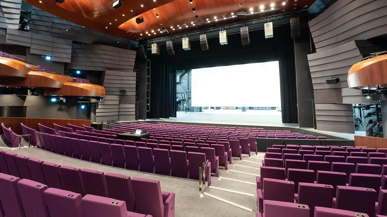 Modern theater interior featuring purple seating, a large stage with a screen, and wooden accents on the ceiling.