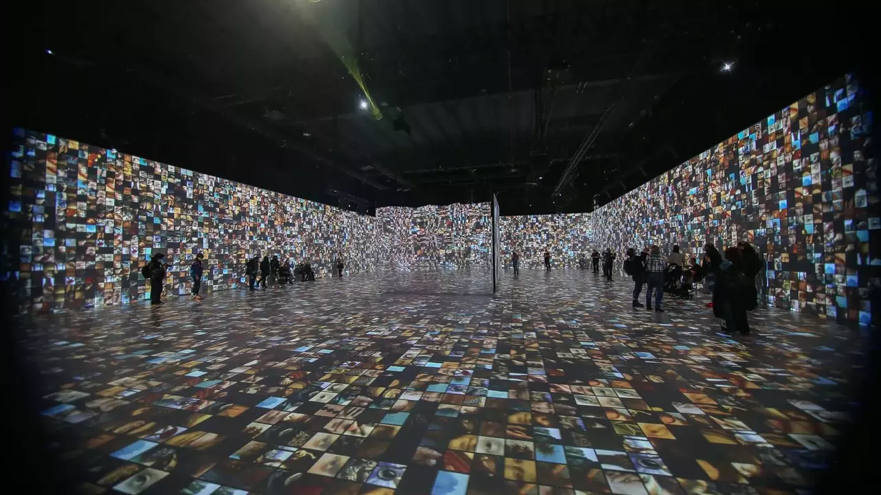 A large exhibition space filled with numerous digital images displayed on walls and the floor, with attendees exploring the installation.