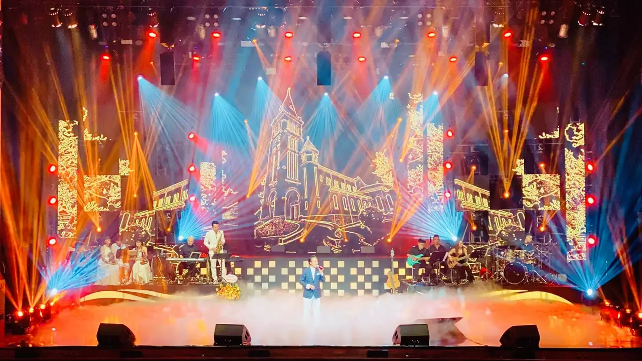 Eine lebendige Bühne mit bunten Lichtern und Rauch zeigt einen Darsteller vor einer Band, vor einem Hintergrund aus beleuchteten architektonischen Designs.