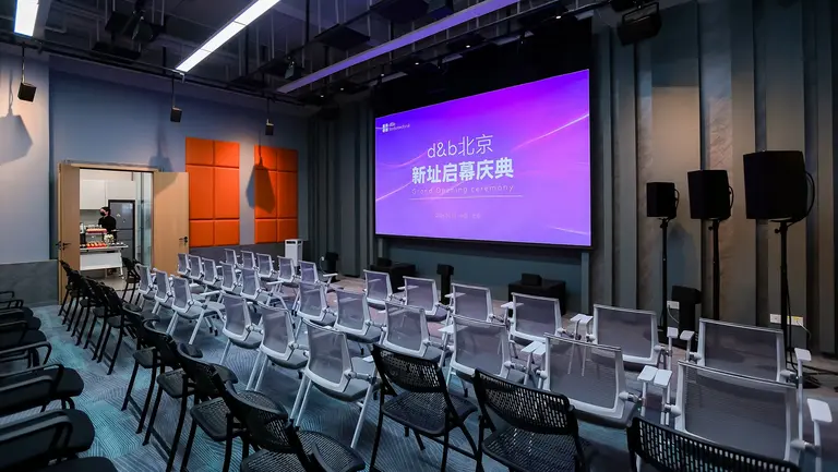A modern conference room with rows of white chairs facing a large screen displaying event details in Chinese.