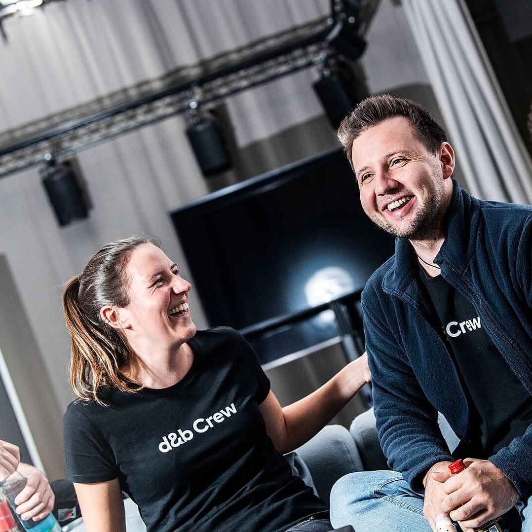 Three people in casual attire, wearing matching black shirts, engage in conversation and laughter in a relaxed indoor setting.