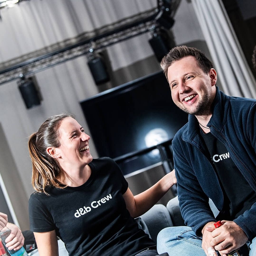 Three people in casual attire, wearing matching black shirts, engage in conversation and laughter in a relaxed indoor setting.