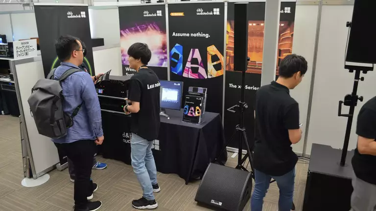 Attendees interact at a booth showcasing audio equipment, featuring displays and promotional materials.